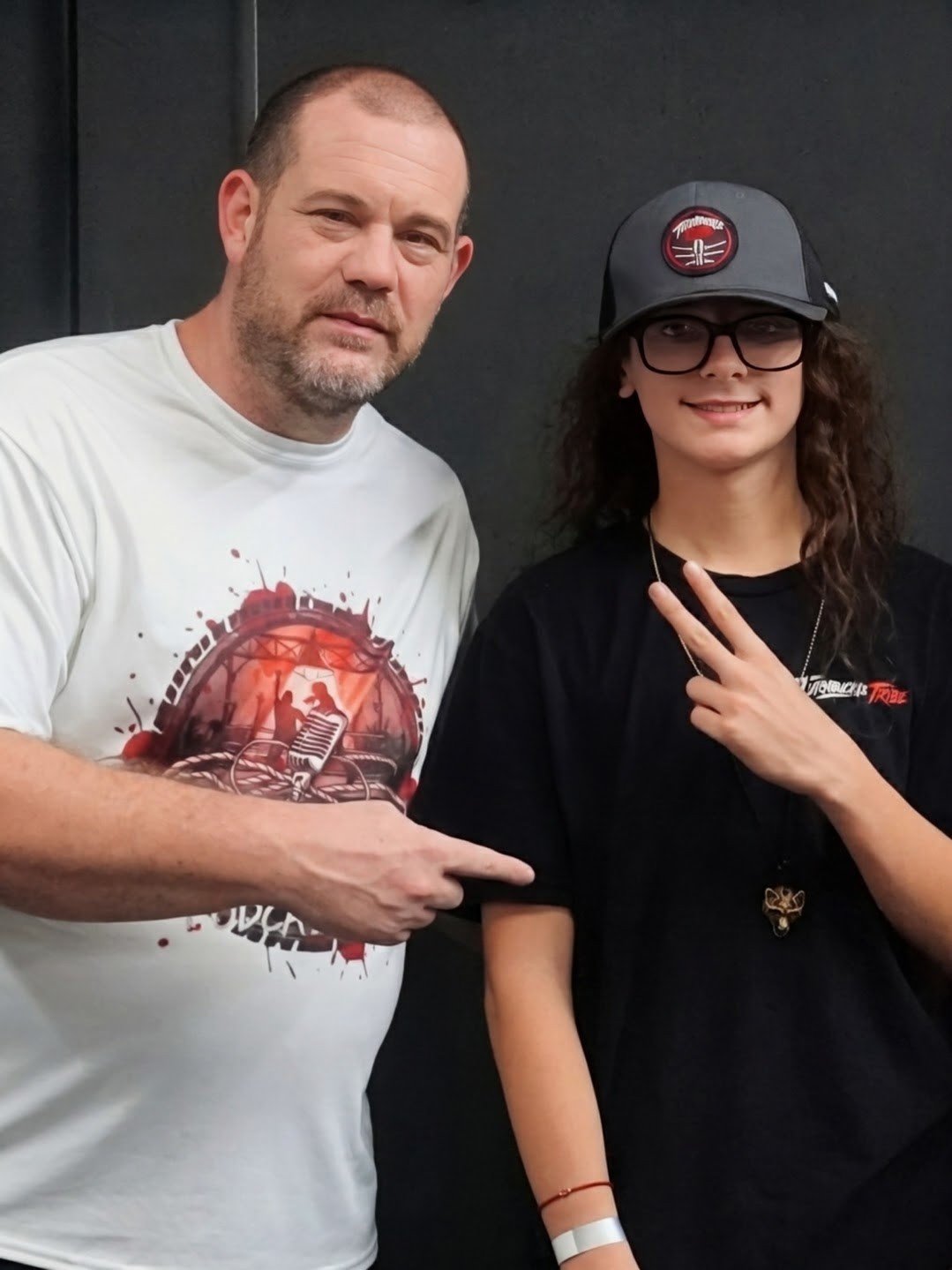 Chris Page of CCP Podcasting pointing to Trystan, who wears a Turnbuckle Tribe cap and shirt and flashes a peace sign