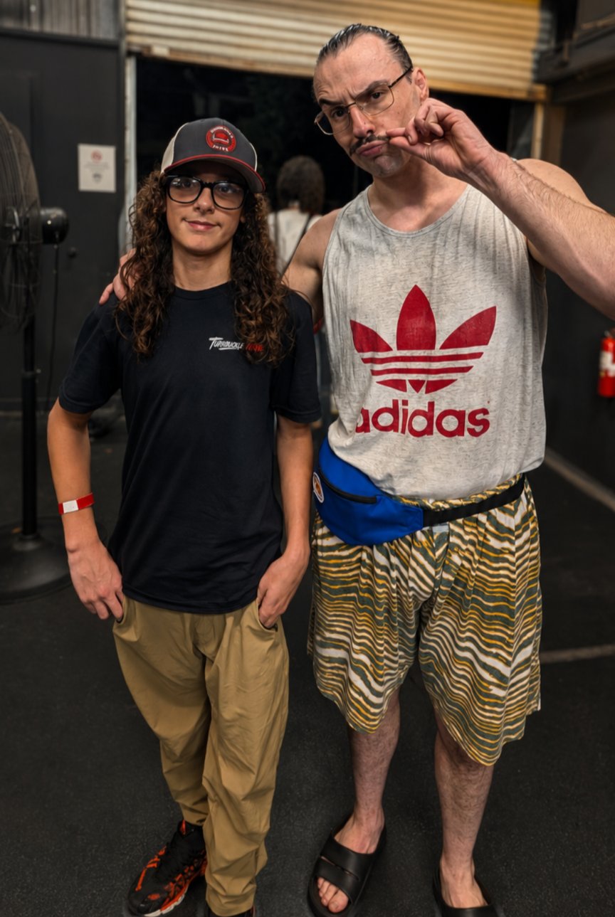 Trystan in his Turnbuckle Tribe shirt and cap posing backstage with wrestler Terry Kid at CCP Podcasting