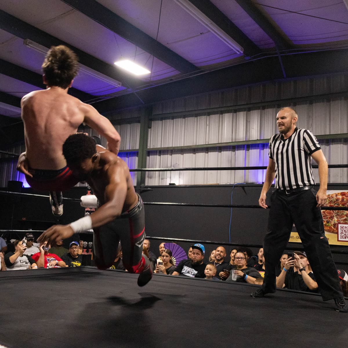 MCG lifting an opponent during a live independent wrestling match as the referee looks on