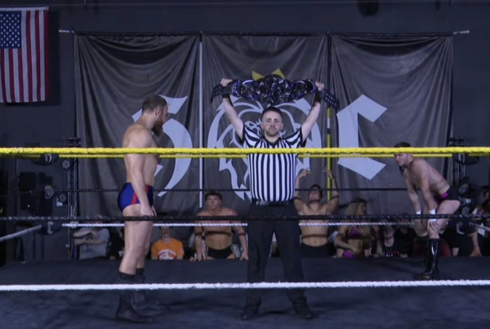 Referee David Sanderson raising a championship belt between two wrestlers before a live match