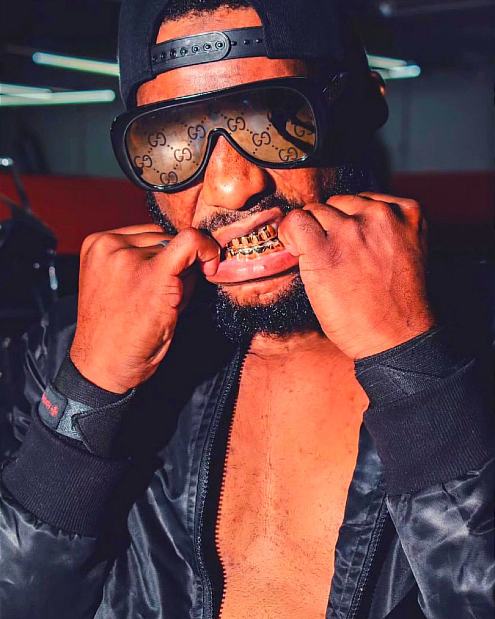 Skrilla The Great wearing sunglasses and a backwards cap while adjusting his grill
