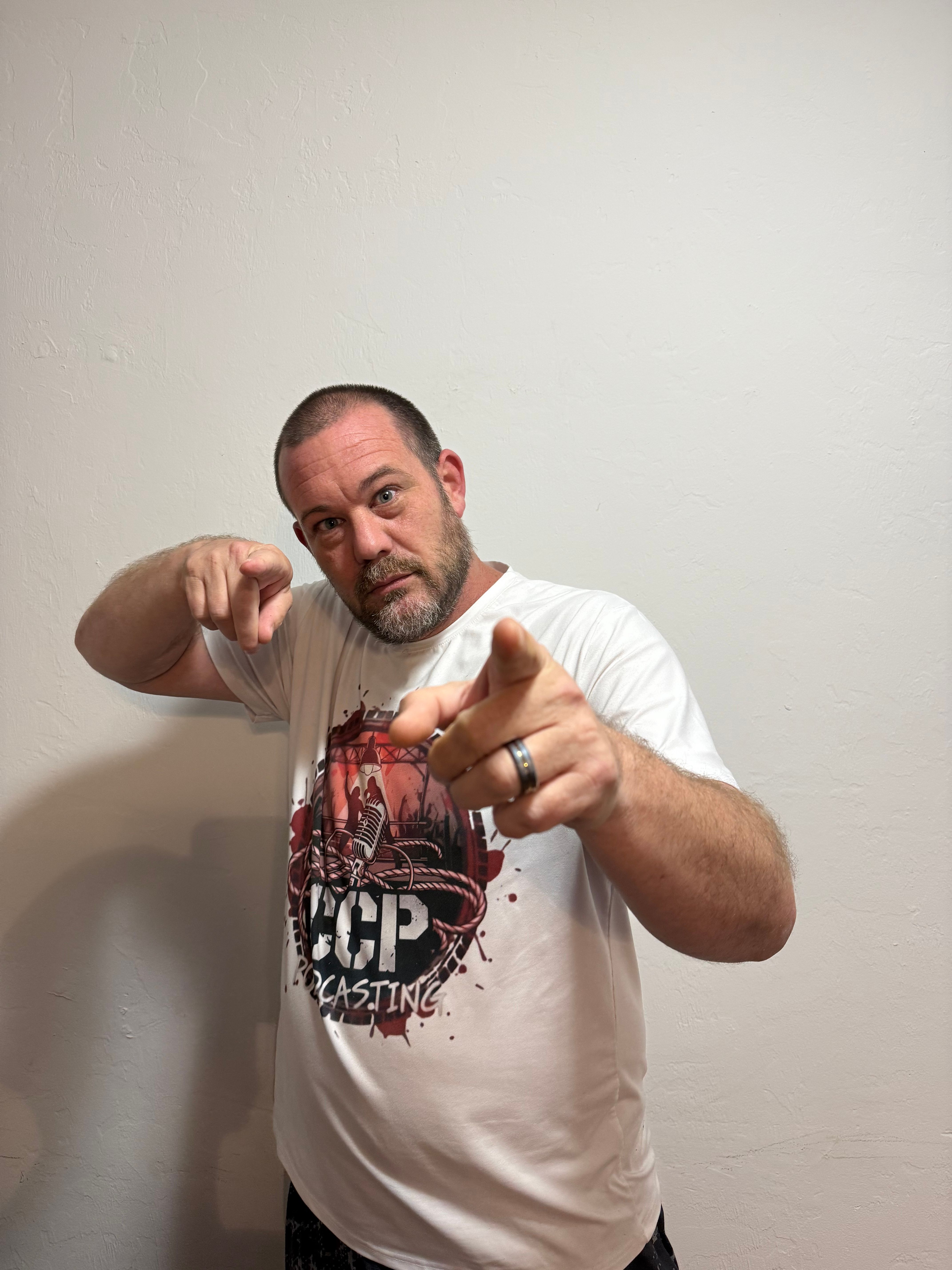 Chris Page pointing toward the camera in a white CCP Podcasting shirt