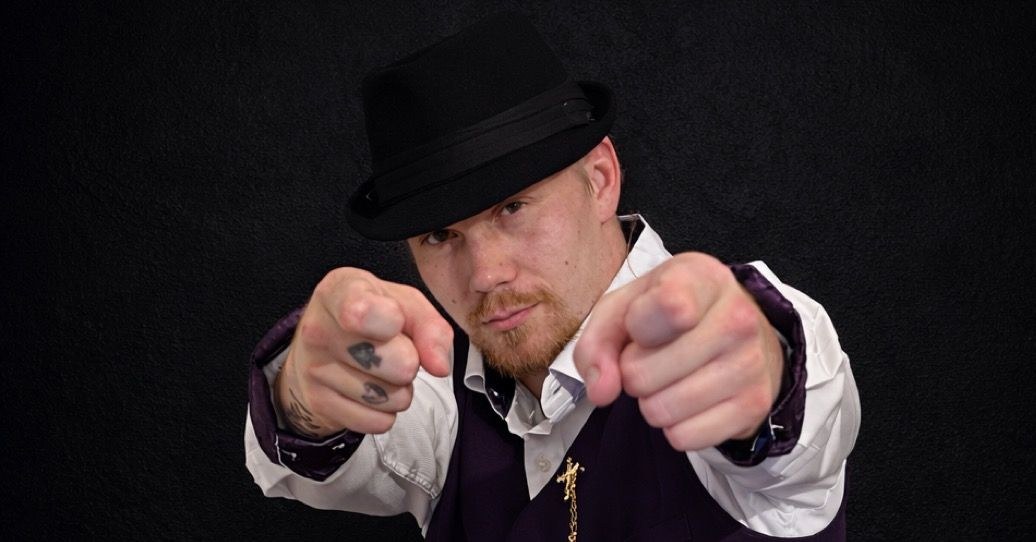 The Don Papa Gill in a black fedora and purple vest pointing both fists at the camera